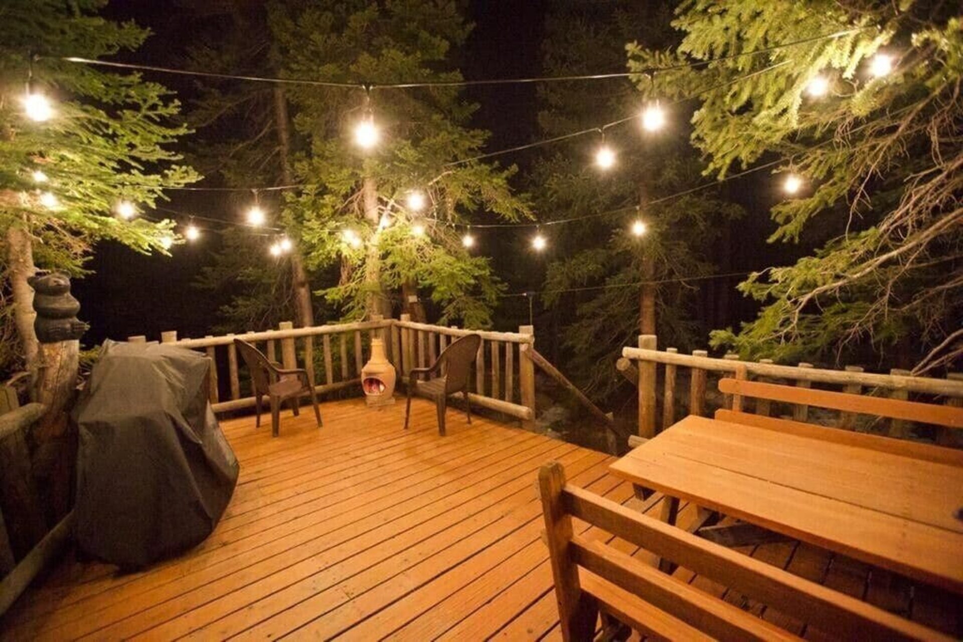 String-lit deck at Kokand Cabin at night, surrounded by pine trees