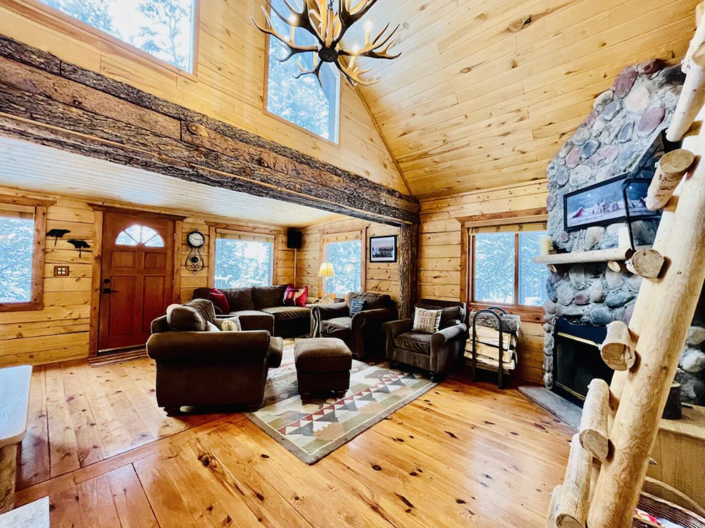 Living room inside Kokand Cabin with stone fireplace, antler chandelier, and vaulted log ceiling